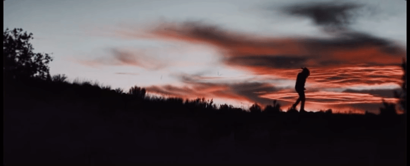 A silhouetted figure walks across a ridge at sunset