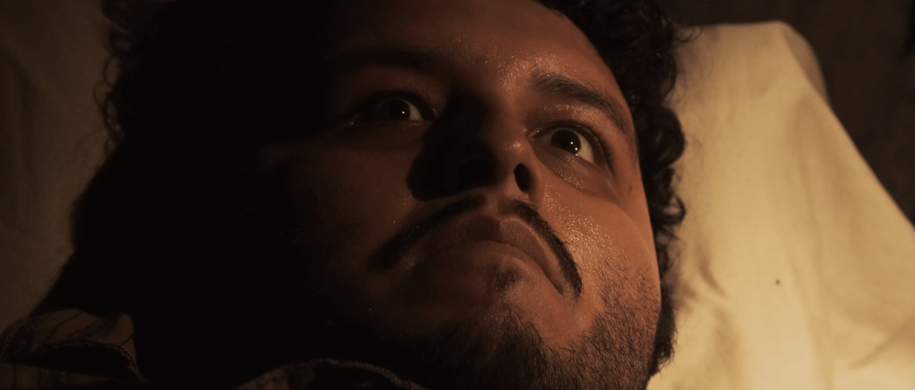 A man lies on a pillow, eyes wide in the dark